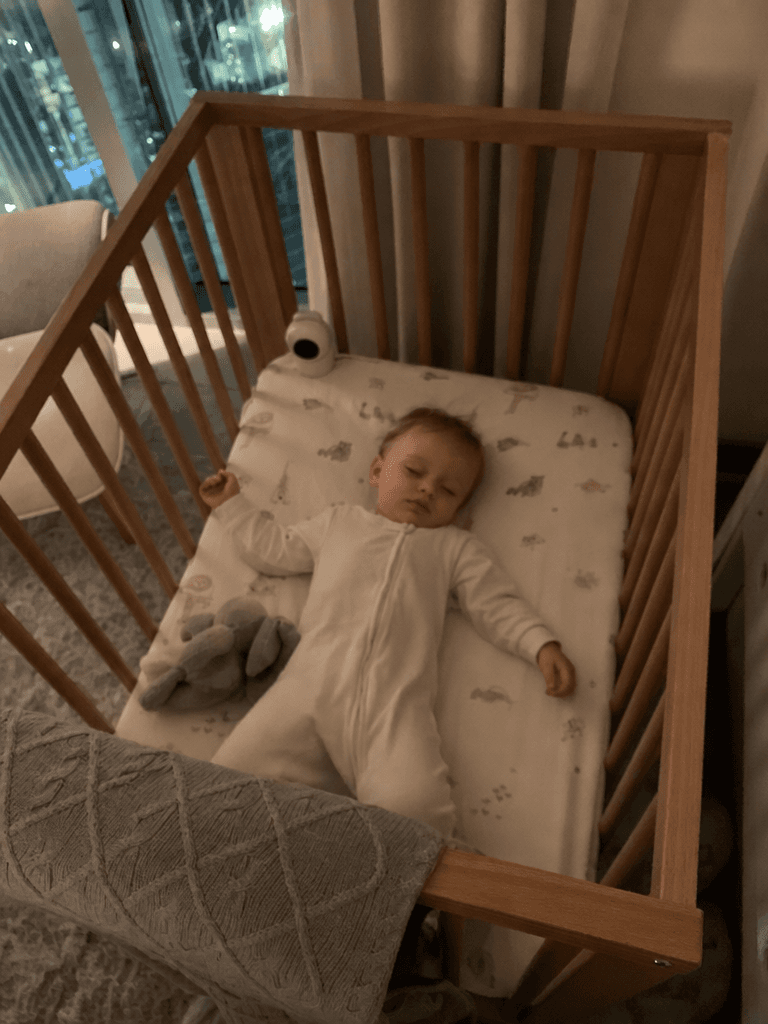 A baby sleeping peacefully on his back in a wooden crib, viewed from above through the rails