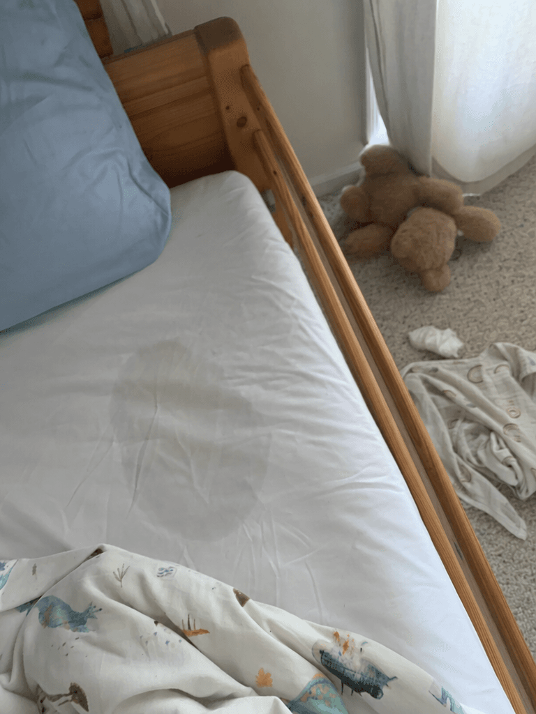 A wet patch soaking through a white cotton fitted sheet on a child's small bed, taken quickly with a phone